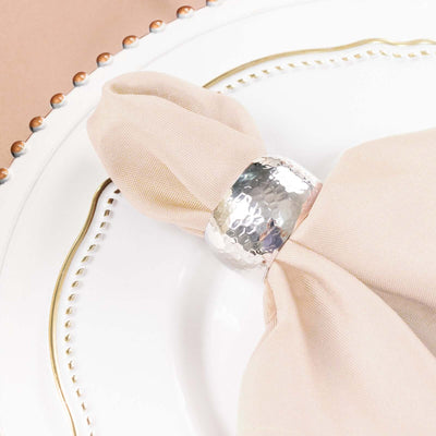 Silver hammered napkin ring on a beige napkin on an elegant plate.