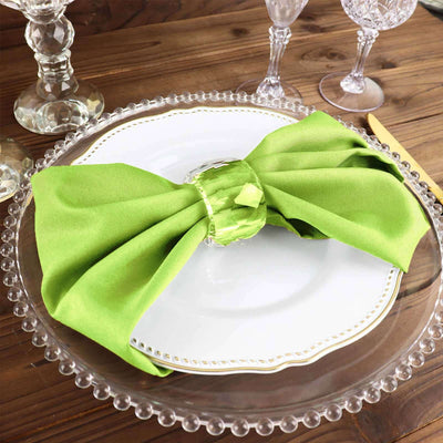 Green napkin tied with a ring on a decorative plate set on a wooden table.