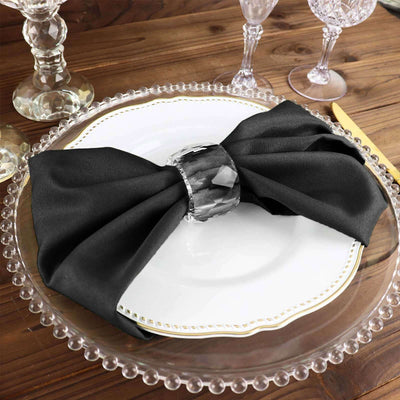Elegant black napkin tied with a crystal napkin ring on a decorative plate.
