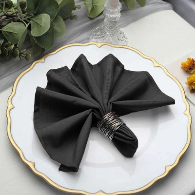 Black napkin elegantly folded on a decorative plate with a silver napkin ring.