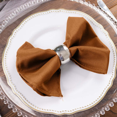 Brown fabric napkin tied with a silver napkin ring on a decorative plate.
