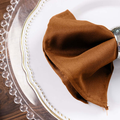 Brown linen napkin elegantly draped over a silver napkin ring on a decorative plate.