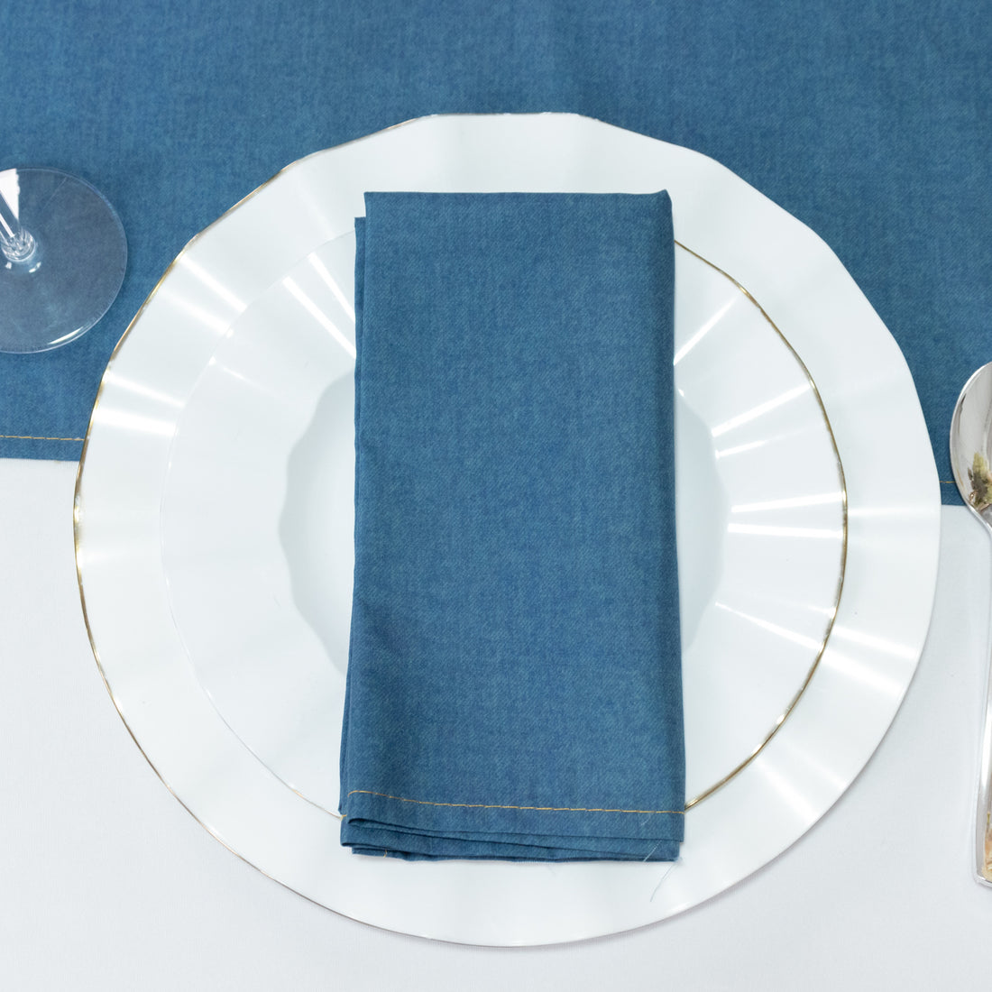 Blue cloth napkin neatly folded on a white plate with gold trim.