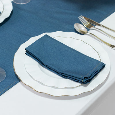 Blue napkin on a decorative white plate with gold trim on a table setting.