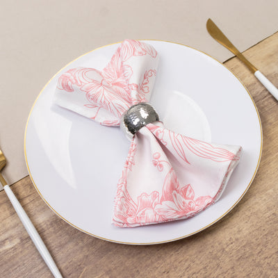 Pink floral napkin tied with a silver ring on a white plate.