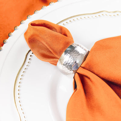 Silver napkin ring on an orange napkin atop a decorative plate.