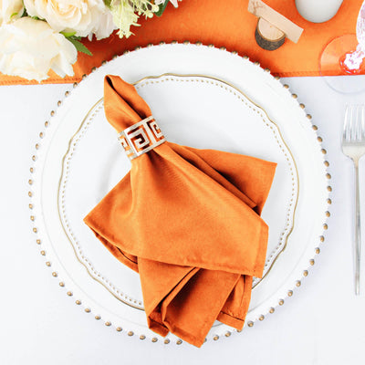 Elegant orange napkin with decorative ring on a white plate.