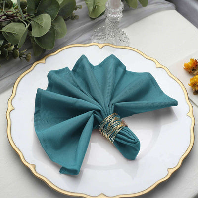 Teal napkin elegantly folded and secured with a gold ring on a decorative plate.