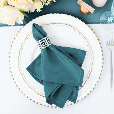 Teal napkin with decorative ring on elegant dinner plate setting.