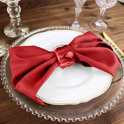 Elegant red napkin tied on a white plate with crystal glassware on a wooden table.