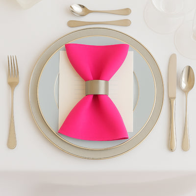 Pink napkin bow on elegant dinner plate setting with silver cutlery.