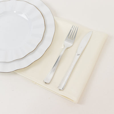 Elegant white dinner plate with gold rim, silver fork, and knife on cream napkin.