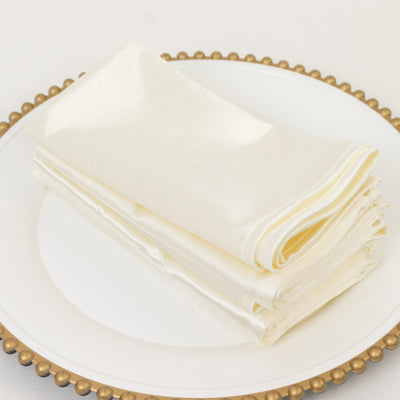 Cream satin napkins stacked on a decorative plate.