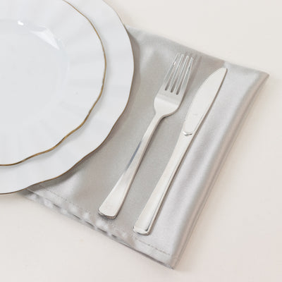 Elegant white plate with gold rim, fork, and knife on a silver napkin.