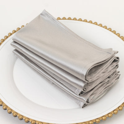 Silver satin napkins neatly folded on a decorative plate.