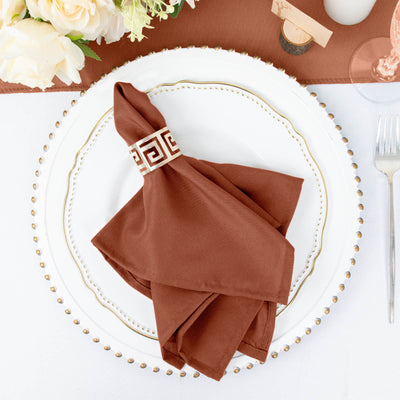 Brown napkin with decorative band on elegant plate setting.
