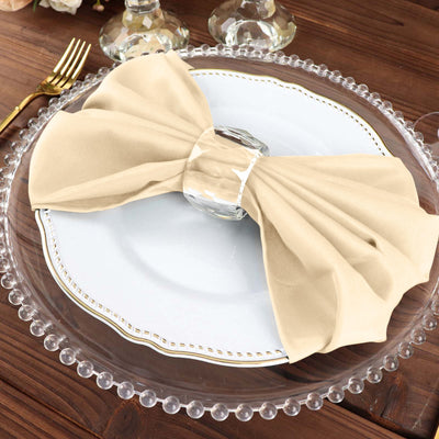 Elegant beige napkin tied with glass ring on a decorative plate.