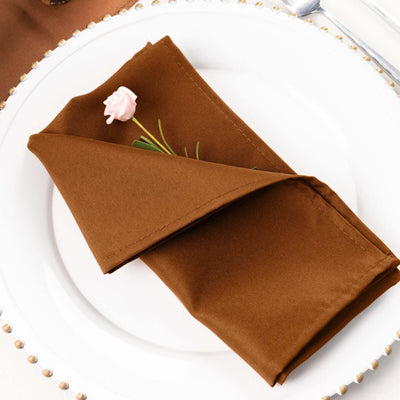 Brown napkin elegantly folded on a white plate with a pink flower accent.