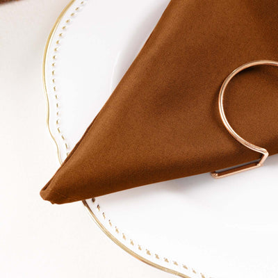 Brown napkin with a rose gold napkin ring on a decorative plate.