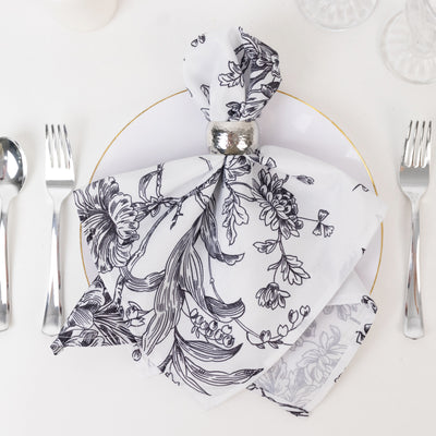 Elegant floral napkin with silver ring on a white plate setting.