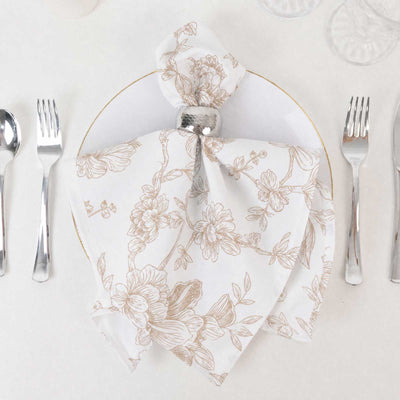 Elegant floral white napkin folded on a gold-rimmed plate with silverware