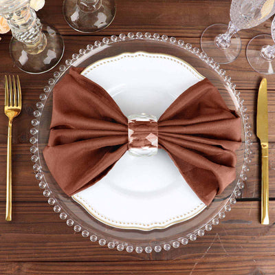 Brown napkin bow on elegant dinner plate with glassware and cutlery.