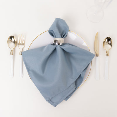Blue napkin elegantly arranged on a white plate with gold-edged trim and silver cutlery.