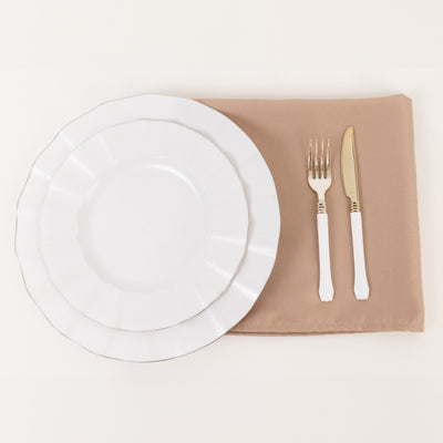 Elegant white dinner plates with gold-accented cutlery on a beige napkin.