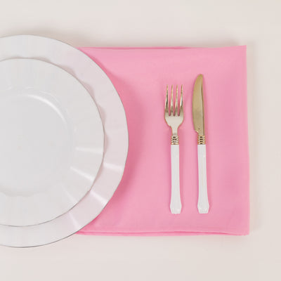 White dinner plate, fork, and knife on a pink napkin.