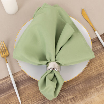 Green napkin with silver ring on a white plate, gold utensils on wooden table.