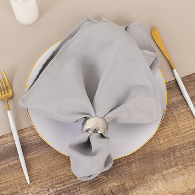 Gray napkin tied with a silver ring on a white plate, set on a wooden table.
