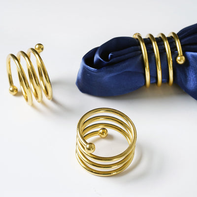 Gold spiral napkin rings on a blue napkin.
