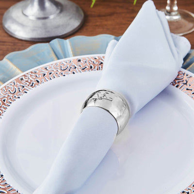 Silver napkin ring on a blue napkin placed on a decorative plate.