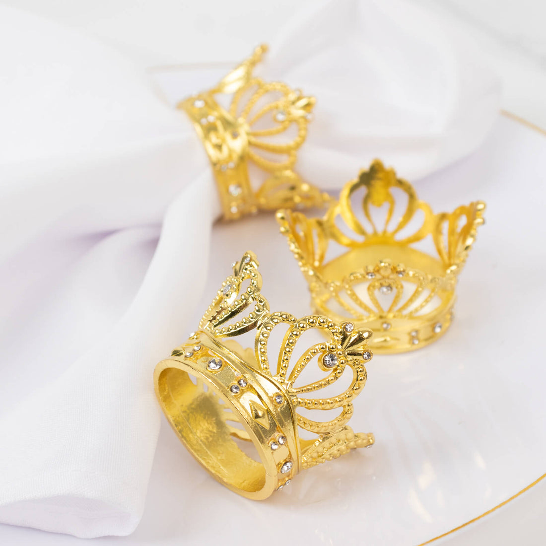 Gold crown napkin rings on a white table setting.