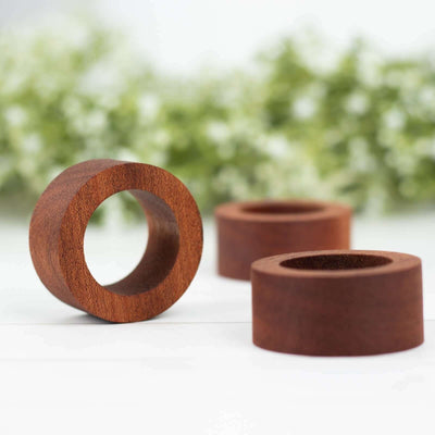 Wooden ring holders in various sizes on a blurred floral background.
