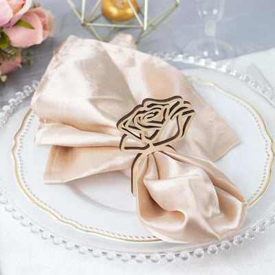Rose napkin holder on a satin napkin, elegantly arranged on a decorative plate.