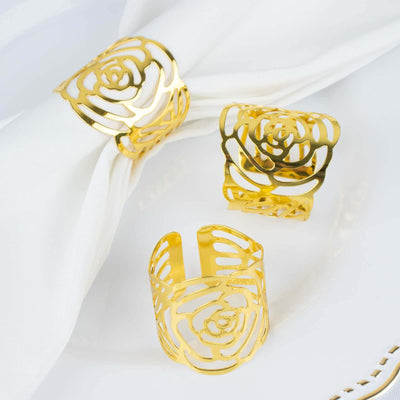 Gold rose napkin rings set on a white tablecloth.