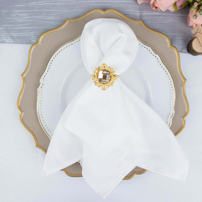 Elegant white napkin tied with a gold brooch on a decorative plate.