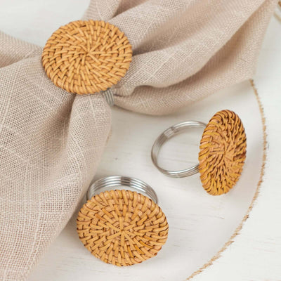 Woven rattan napkin rings set on a light fabric backdrop.