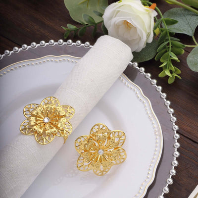 Elegant gold flower napkin rings on a decorative plate with a floral accent.