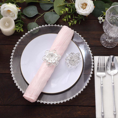 Elegant table setting with pink napkin and floral napkin ring on a decorative plate.
