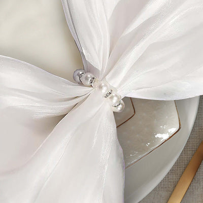 Elegant white napkin ring with pearl accents on a dining table setting.