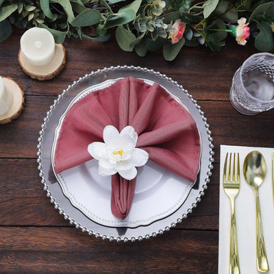 Elegant maroon napkin with a white flower on a decorative plate, styled for a table setting.