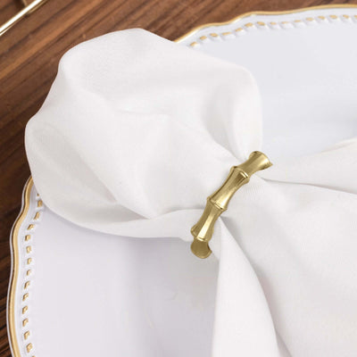 Gold bamboo napkin ring on a white napkin atop a decorative plate.