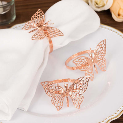 Rose gold butterfly napkin rings on a white plate with a napkin.