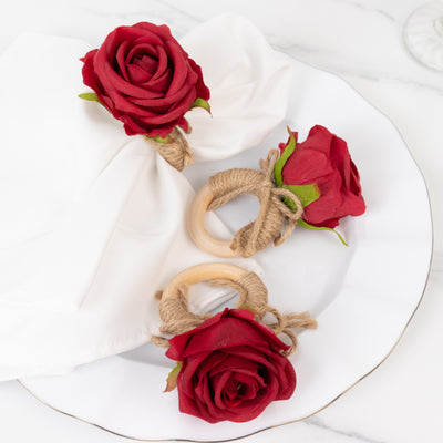 Red rose napkin rings on a white plate with a napkin.