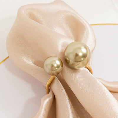 Gold pearl napkin rings on elegant satin fabric.
