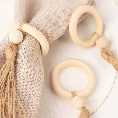 Natural wood napkin rings with tassel accents on a neutral fabric.