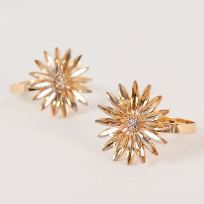Gold flower-shaped earrings with sparkling details on a neutral backdrop.