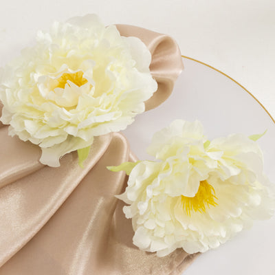Two ivory peony flowers on a silk napkin and plate.